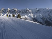 some skiers going down the slope of a snow covered mountain peak, with a blue sky above them