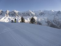 some skiers going down the slope of a snow covered mountain peak, with a blue sky above them