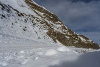 a man riding skis on a snow covered slope next to a steep cliff formation