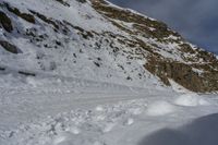 a man riding skis on a snow covered slope next to a steep cliff formation