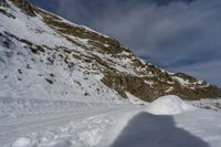 a man riding skis on a snow covered slope next to a steep cliff formation