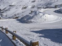 a wooden fence near a mountain covered in snow and a person skiing down the slope