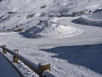 a wooden fence near a mountain covered in snow and a person skiing down the slope