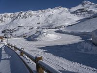 a wooden fence near a mountain covered in snow and a person skiing down the slope