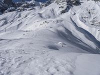 a man riding skis across a snow covered slope covered in snow next to mountains