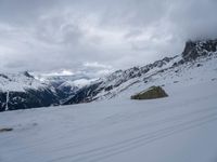 a person skiing down a snow covered slope with mountains in the background with clouds and rocks