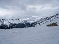 a person skiing down a snow covered slope with mountains in the background with clouds and rocks