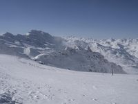 a person skiing down a ski slope surrounded by snowcapped mountains and trees on a sunny day