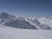 a person skiing down a ski slope surrounded by snowcapped mountains and trees on a sunny day