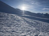 a person is walking along the snow covered ground with ski poles, in front of sun shining through mountains