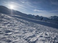 a person is walking along the snow covered ground with ski poles, in front of sun shining through mountains