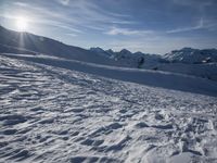 a person is walking along the snow covered ground with ski poles, in front of sun shining through mountains