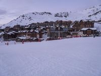 a snow covered mountain with some buildings and ski tracks in the middle of it and people in the front