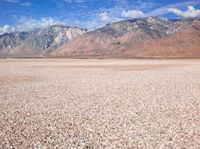 a barren field with small rocks around it with a mountain in the background that is covered in snow