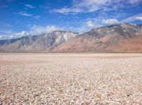 a barren field with small rocks around it with a mountain in the background that is covered in snow