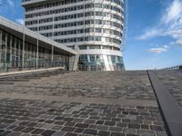 large circular building on a high floor in front of a glassy building with a blue sky