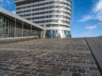 large circular building on a high floor in front of a glassy building with a blue sky