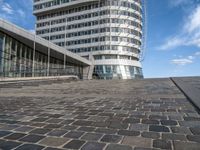 large circular building on a high floor in front of a glassy building with a blue sky