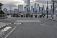 a paved park with benches next to a water body and a skyline of high rises in the background
