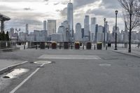 a paved park with benches next to a water body and a skyline of high rises in the background