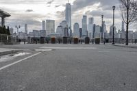 a paved park with benches next to a water body and a skyline of high rises in the background