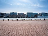 a brick sidewalk near water with a view of a river and tall buildings in the background