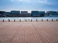 a brick sidewalk near water with a view of a river and tall buildings in the background