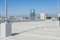 an empty parking lot is seen with the city in the distance across from the water tower