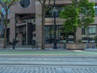 the green paint is painted on a bike path in front of an office building and large, trees