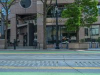 the green paint is painted on a bike path in front of an office building and large, trees