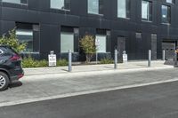 two cars parked near a parking lot near a black building with a sign indicating parking meters