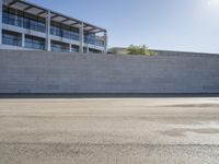 a man rides a skateboard on the pavement outside an office building with a wall