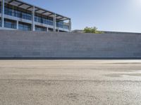 a man rides a skateboard on the pavement outside an office building with a wall