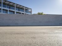 a man rides a skateboard on the pavement outside an office building with a wall