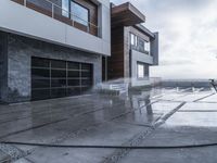 a person that is washing the cement in the driveway while another man is standing in front of a building