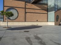 a parking area with a tree next to the entrance of a large building covered in brick walls