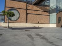 a parking area with a tree next to the entrance of a large building covered in brick walls