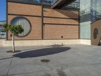 a parking area with a tree next to the entrance of a large building covered in brick walls