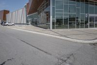 a long building with glass doors next to a street and cars driving by them on the other side