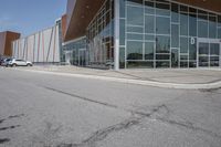 a long building with glass doors next to a street and cars driving by them on the other side