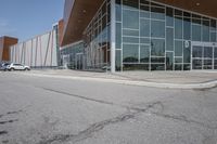 a long building with glass doors next to a street and cars driving by them on the other side