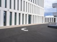 a paved parking lot with an open white building to the side and a white circle at the end