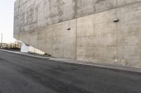 a man in a white shirt and black pants is skate boarding on the side of a gray concrete building