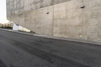 a man in a white shirt and black pants is skate boarding on the side of a gray concrete building