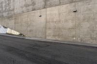 a man in a white shirt and black pants is skate boarding on the side of a gray concrete building