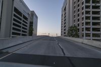 a empty city street with cars going past by buildings and skyscrapers and sun coming up