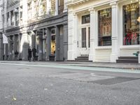 a small dog walking on a sidewalk with two people watching him as another person walks