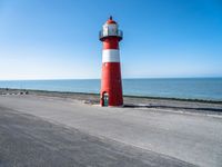 a small lighthouse on the beach near some water and cars in traffic passing by and a blue sky