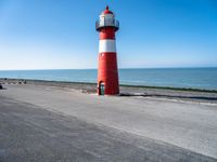 a small lighthouse on the beach near some water and cars in traffic passing by and a blue sky