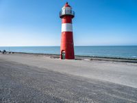 a small lighthouse on the beach near some water and cars in traffic passing by and a blue sky